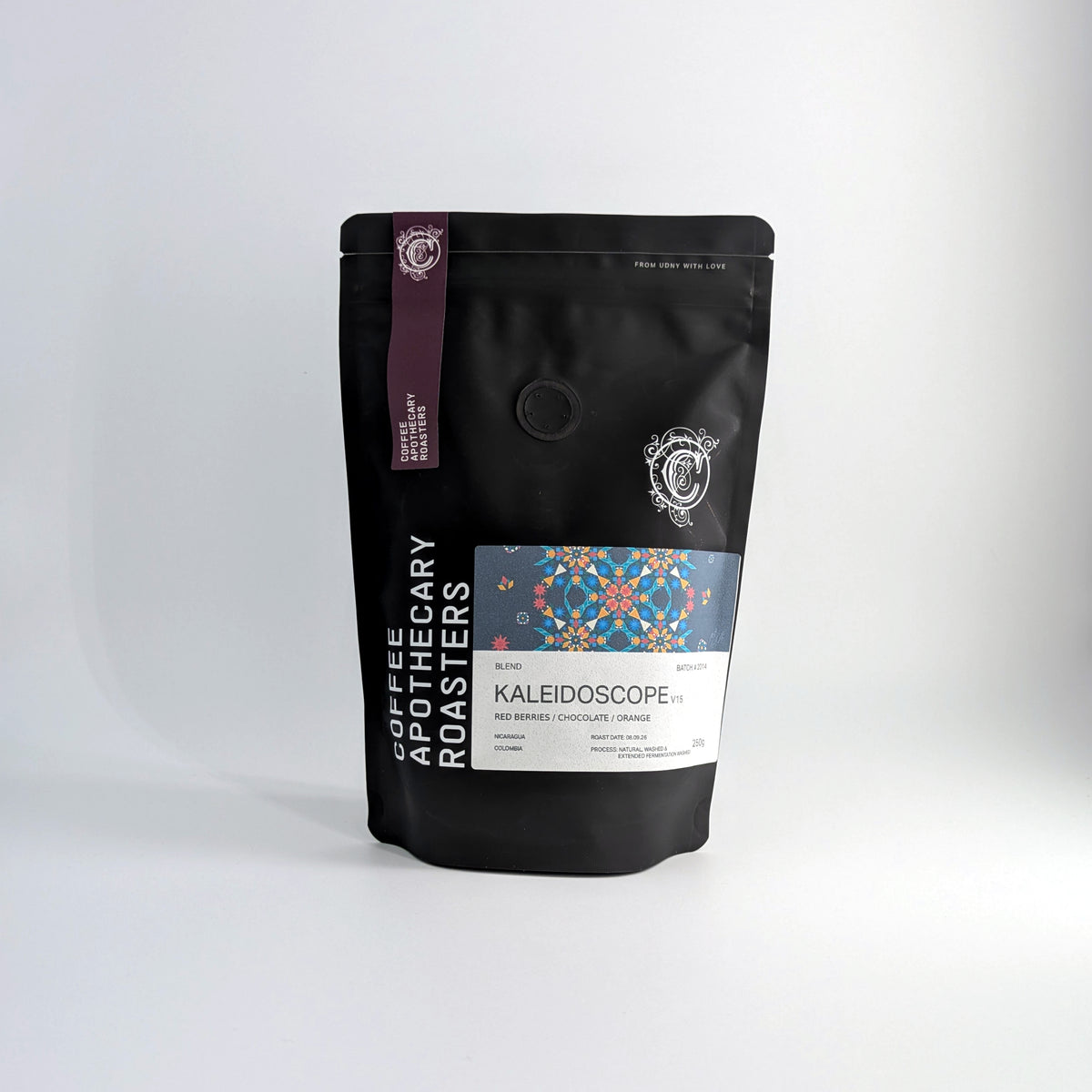 A black stand-up pouch of Coffee Roastery Kaleidoscope blend coffee beans, featuring a colorful geometric label and a purple vertical stripe, set against a clean white studio background.